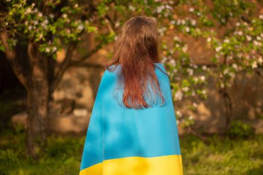 The girl is standing behind the camera with the Ukrainian flag on her back. Yellow and blue fabric.