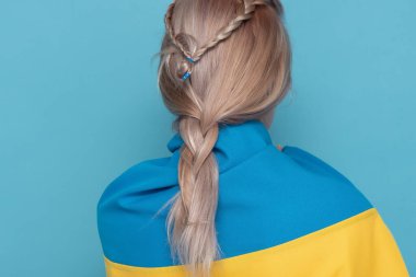 Kadın mavi arka planda kameraya geri döndü. Omuzlarında mavi-sarı kumaş olan bir kadın..