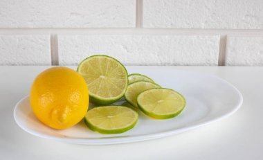 Limon, limon, sulu olgun narenciye meyveleri mutfak arka planında beyaz bir tabakta. Serinletici içecekler ve Mojito kokteylleri yapmak için gerekli malzemeler. Metnin için yer.