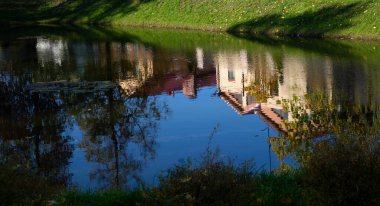 Bitkilerin, ağaçların ve kristal berrak sudaki evlerin yansıması. Gölgeli bir göletin kıyısında. Güneşli bir gün. Sonbahar.