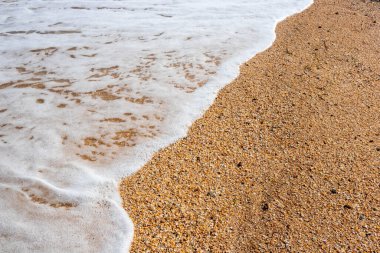 Kumsalın arka planında beyaz köpük dalgası.