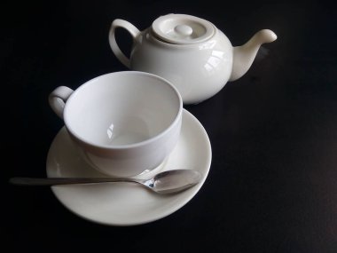 Beyaz fincan, çay tabağı ve çaydanlık siyah arka planda izole edilmiş..
