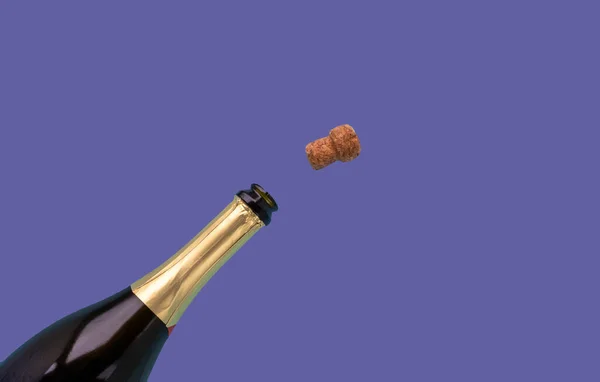 A bottle of champagne and a cork are open on a very peri lilac background.