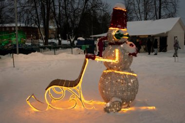 In the evening park, a glowing snowman on a winter sleigh.