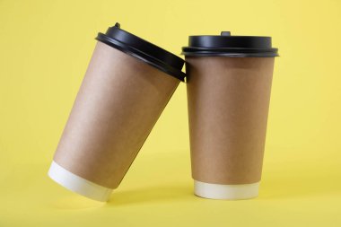 Two brown glasses with lids on a yellow background.