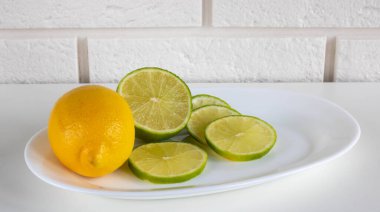 Fresh lime cut into slices and lemon on a white plate.