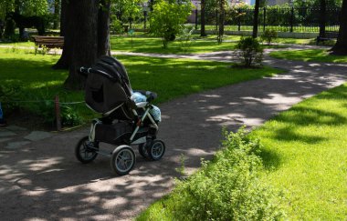 A baby carriage stands alone in the park on a bright summer day.