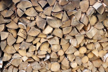 A beautiful closeup view of cut and split firewood stacked outdoor up against a shed under roof.
