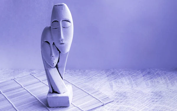 A statuette of a couple isolated on a lilac background very peri. The face of a man and a woman. place for your text.