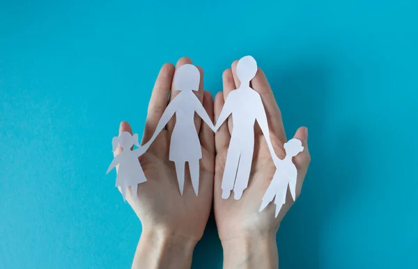 Mavi arka planda kağıt bir aileyi tutan eller. Aile Günü, Kardeşler Günü, İnsan Hakları Günü, Dünya Barış Günü.