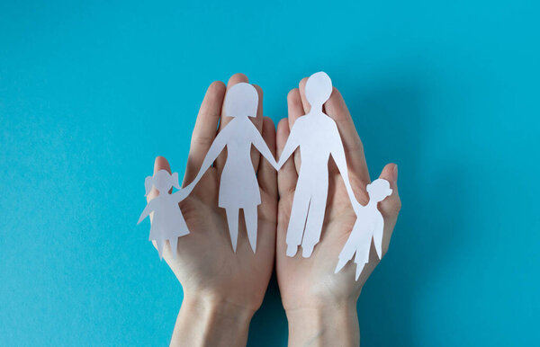 Hands holding a paper family on a blue background. The concept of Family Day, Brothers and Sisters Day, Human Rights Day, World Peace Day.