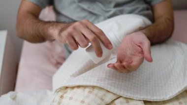 Asyalı bir adam evde yatak odasındayken avucunun içine haplar alıyor..