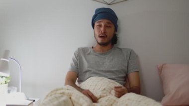 Asyalı adam evdeki yatak odasında hasta bir şekilde öksürüyor. Genç erkek sağlığı ve sağlık hizmetleri.