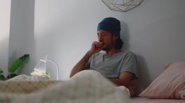 Asyalı adam hasta öksürüyor ve yatak odasındayken avucunun içine haplar alıyor. Genç erkek sağlığı ve sağlık hizmetleri.