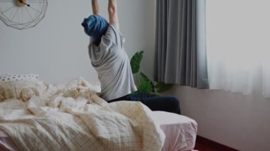 Çekici Asyalı bir adam uyanır ve yatak odasında yatakta uzanır. Sabah güneşi evin penceresinden parlar..