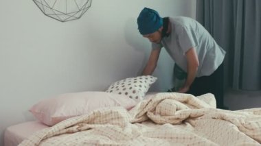 Çekici bir Asyalı erkek dışarı çıkmadan önce yatak odasında yastıklar düzenler. Sabah güneşi evdeki pencereden parlıyor..