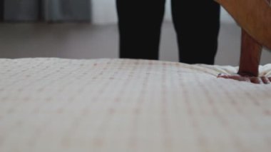 Yatak odasındaki yatak örtüsüne dokunan eller yastıkları düzenler. Sabah güneşi evdeki pencereden parlıyor..