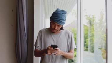 Ciddi bir Asyalı serbest yazar. Evdeki ofisin penceresinin yanında dikilirken akıllı telefonuna mesaj yazıyor..