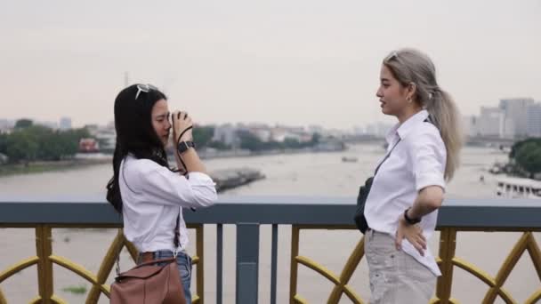 橋の上に立っていると幸せなアジアのレズビアンカップルが写真を撮っています 友人の休暇のライフスタイルで旅行する美しいアジアの女性 — ストック動画