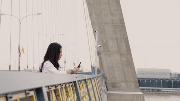 橋の上に立っている間 スマートフォンを使ってウェブサイトを閲覧している美しいアジアの女性 アジアの女性旅行休暇のライフスタイル — ストック動画