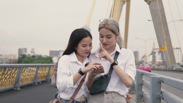 橋の上に立っている間 スマートフォンを使ってウェブサイトを閲覧しているアジアのレズビアンカップル ローアングルショット — ストック動画