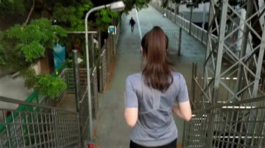 Şehirdeki bir üst geçitte müzik dinleyen, kulaklık takan genç ve güzel Asyalı bir bayan sporcu. Antrenman kardiyo koşu yaşam tarzı gün batımında sokakta..