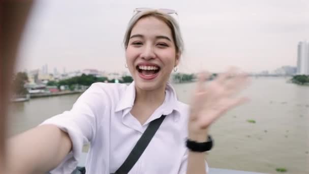 タイのラーマ8世橋の上に立っている間に彼女の友人とチャット若いアジアの女性のビデオのビューのショット — ストック動画