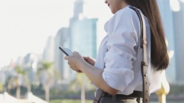 Kapalı eller beyaz gömlekli Asyalı iş kadını akıllı telefon kullanıyor sosyal medyada mesajlaşırken bir yandan da halk parkında mesajlaşıyor..