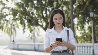 Beyaz tişörtlü genç Asyalı iş kadını, sosyal medyada mesajlaşarak akıllı telefon kullanıyor..