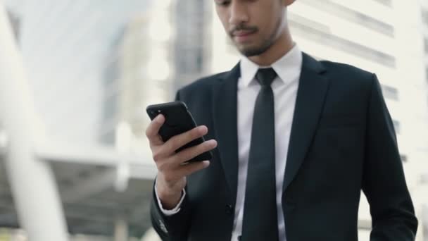 スマートフォンでソーシャルメディアを閲覧し オフィスの従業員にメッセージを送信することで 魅力的なアジアのビジネスマン — ストック動画