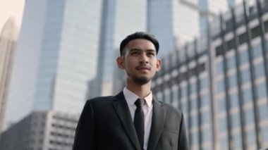 Başarılı bir Asyalı işadamı, sabah büyük bir ofis binasının yanında caddede dururken mutlu bir şekilde iyi haberi kutluyor..