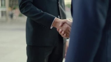 Siyah takım elbiseli Asyalı iş adamlarını yakalayın. Sokakta büyük bir ofis binasının yanında dururken ortaklık anlaşması yapın..