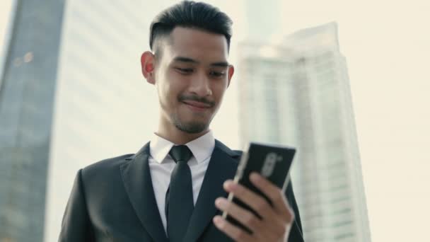 スマートフォンのテキストメッセージをオンラインで確認し 路上都市に立っている間 ソーシャルネットワークを使用して幸せなハンサムな若いビジネスマン — ストック動画