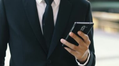 Genç Asyalı işadamı, şehir dışında dururken akıllı telefonuna gün batımı mesajı yazıyor..