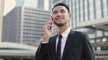 Siyah takım elbiseli çekici bir işadamı caddenin ortasında büyük bir ofis binasının yanında dikilirken telefonla konuşuyor..