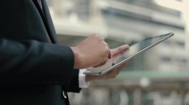 Siyah takım elbiseli yaratıcı bir işadamını dışarıda, büyük bir ofis binasının yanında dururken tabletini kullanarak sosyal medyayı kapatın..