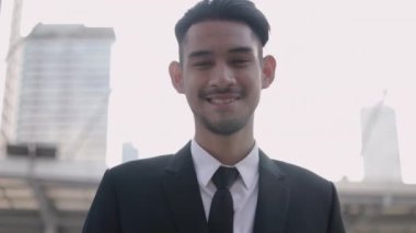 Siyah takım elbiseli, gülümseyen yakışıklı bir işadamının portresi. Sokakta, büyük bir ofis binasının yanında duruyor. Gün batımını seyrediyor..