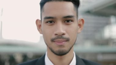 Siyah takım elbiseli, gülümseyen yakışıklı bir işadamının portresi. Sokakta, büyük bir ofis binasının yanında dikilirken..