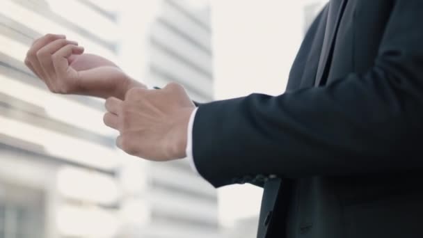 仕事の準備をする黒いスーツに身を包んだアジアのビジネスマンのクローズアップ 大きなオフィスビルの近くの通りの外に立っている間に日没を持っている都市 — ストック動画