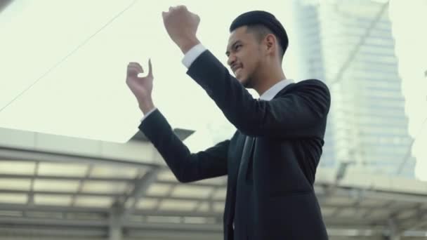 成功したビジネスマンだ アジアの男の勝者は 大規模なオフィスビル都市の近くの通りに立っている間 幸せな喜びを感じる良いニュースを祝う — ストック動画