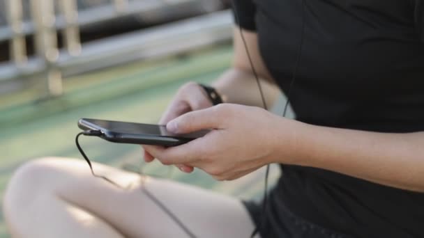 迷人的高加索女运动员坐在城市日落的街道旁边 一边在社交媒体上分享着自己的信息 戴耳机听音乐的女跑步者 — 图库视频影像