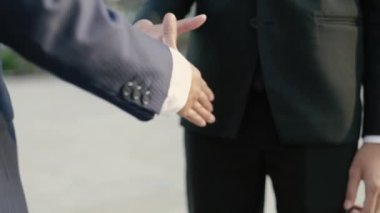 Siyah takım elbiseli Asyalı iş adamları, sokakta büyük bir ofis binasının yanında dururken el sıkışarak ortaklık anlaşması yapıyorlar..