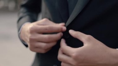 Asyalı işadamının işe hazırlanan siyah takım elbisesini giydiği yakın plan. Sokakta, büyük bir ofis binasının yanında dururken gün batımını seyrederken..