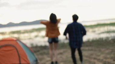 Asyalı kampçılar el ele tutuşarak ve zıplayarak başarılı tırmanış kutlamaları yaparak güneşli ve güzel bir manzara üzerinde kamp kurarak tatil yolculuğunun tadını çıkarıyorlar..