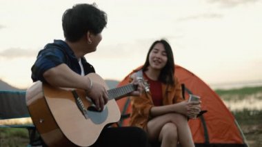 Genç Asyalı mutlu bir çift gitar çalıyor ve tatilde kamp yapmanın yanında şarkı söylüyor..