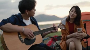 Genç Asyalı mutlu bir çift gitar çalıyor ve tatilde kamp yapmanın yanında şarkı söylüyor..