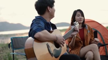 Mutlu bir Asyalı çift, hafta sonu kamp yapmanın yanında gitar çalıp şarkı söylüyor..