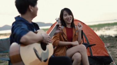 Genç Asyalı mutlu bir çift gitar çalıyor ve tatilde kamp yapmanın yanında şarkı söylüyor..