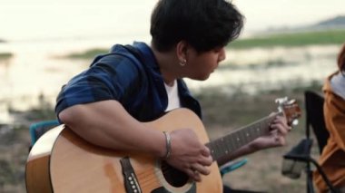 Mutlu bir Asyalı çift kampta kampta dinlenirken gitar çalıp birlikte şarkı söylüyor..