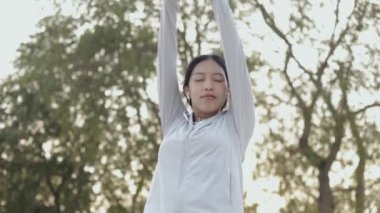 Güzel Asyalı koşucu kadın atlet müzik dinliyor spor kıyafetleri giyiyor kollarını kaldırıyor rahatlamak için hislerini açıyor güneş doğarken sahilde koşuyor sağlıklı yaşam tarzı egzersizleri yapıyor..